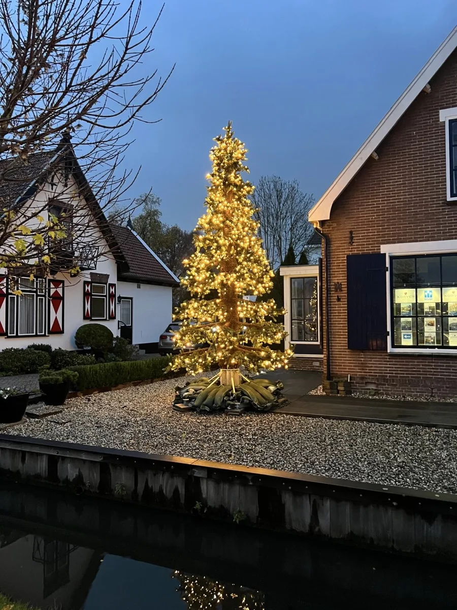 Grote verlichte kerstboom op een stalen voet in een voortuin